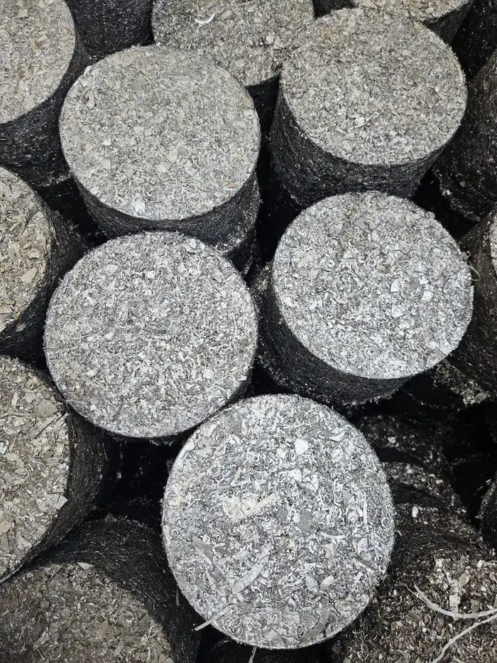 Macro view of briquette end faces, bright compressed metal turnings against dark pressed sides.