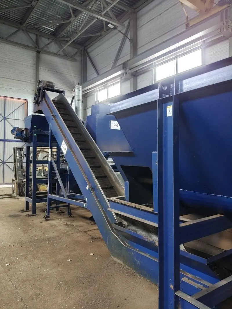 Steel chain conveyor rising at an angle into a large blue receiving hopper marked 12-3.